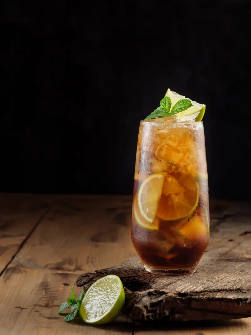 Cuba Libre cocktail drink lavet af coca cola, rom og limesaft, serveret i et glas med limefrugter omkring.