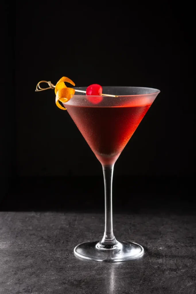 Klassisk Manhatten cocktail mixet af vermouth og whisky, serveret i et højt cocktailglas på en bar.